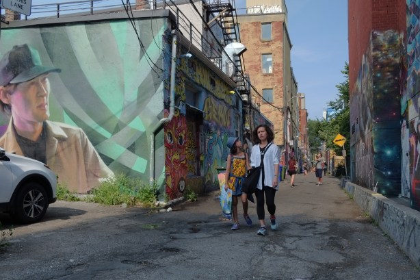 a mother and daughter walk down Graffiti Alley, past a lrge mural of a young man by Janus 