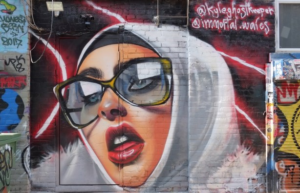 woman wearing a white head scarf and large glasses, with red lips 