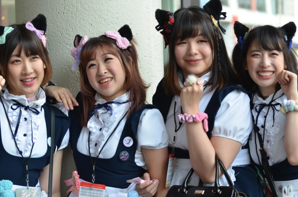 four asian women in navy and white frilly anime french maid costumes, with hair tied up with bows,
