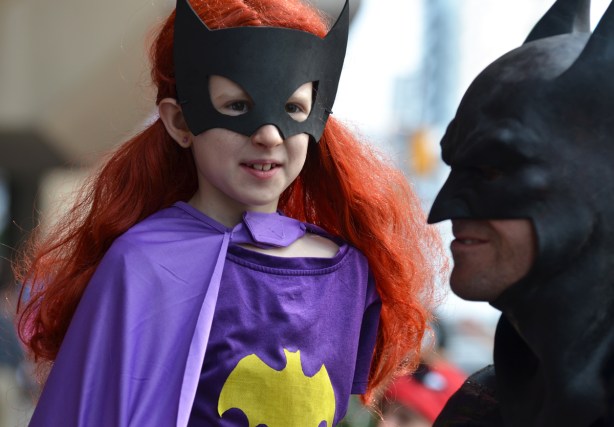 child in long red wig and batman mask, also purple batman costume with a yellow bat symbol, Batman is in the right of the pic