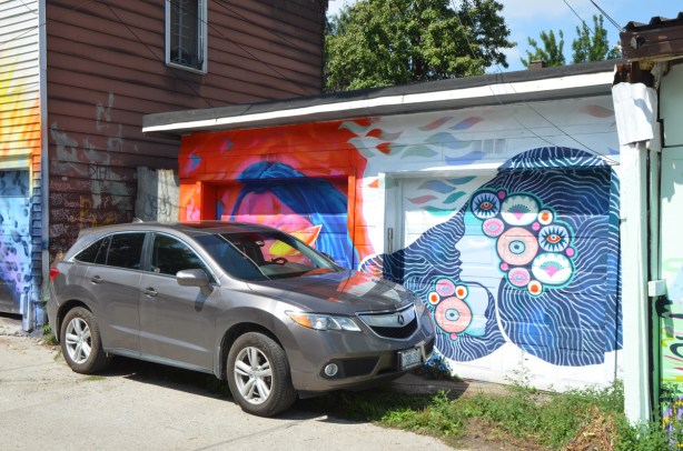 a grey car is parked in front of a double garage, each door has a mural painted on it 