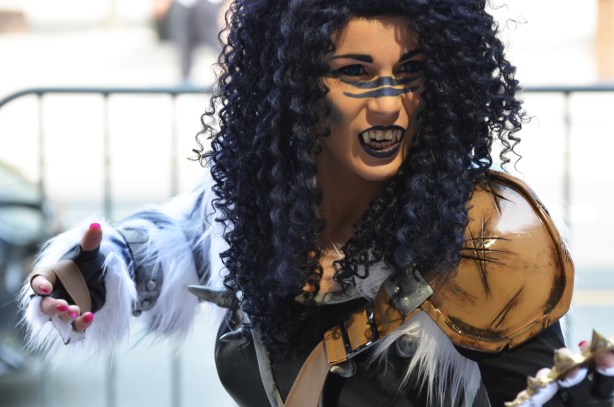 a woman in costume, long curly black hair, fangs, black lips, claws and fur on hands,
