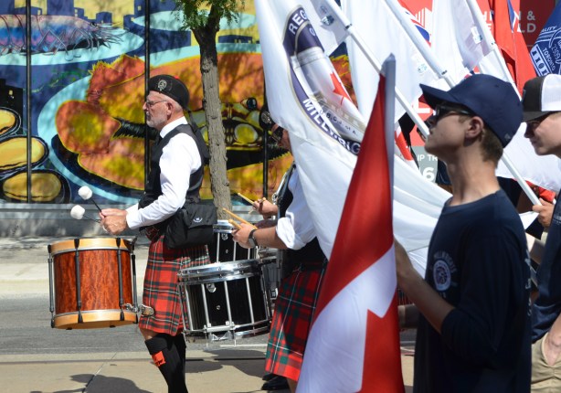 labour Day parade on Queen St West, man in tartan kilt playing drums, union members carrying flags including Canadian flag 