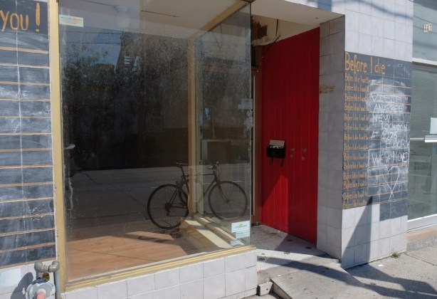 empty store front with a bike parked inside, a red wall beside the door way, dirty glass in front, reflections in the glass 