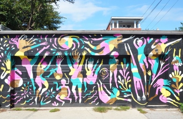 garage front covered with a mural by Erin McCluskey, black background, then figures of women in pink, yellow and pale blue, dancing, playing, flying, jumping, 