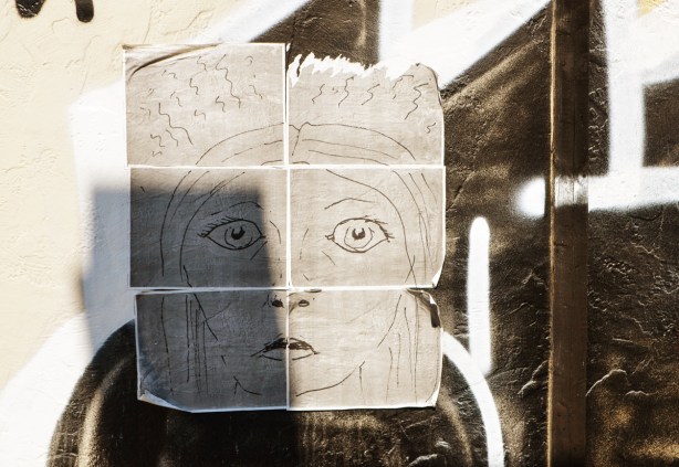 a hand drawn picture of a face, on paper, pasted on a fence