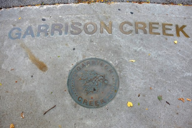 brass letters embedded in the sidewalk that say Garrison Creek, also a round metal medallion with the same words 