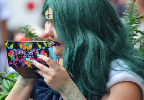 woman with green hair is applying blue lipstick