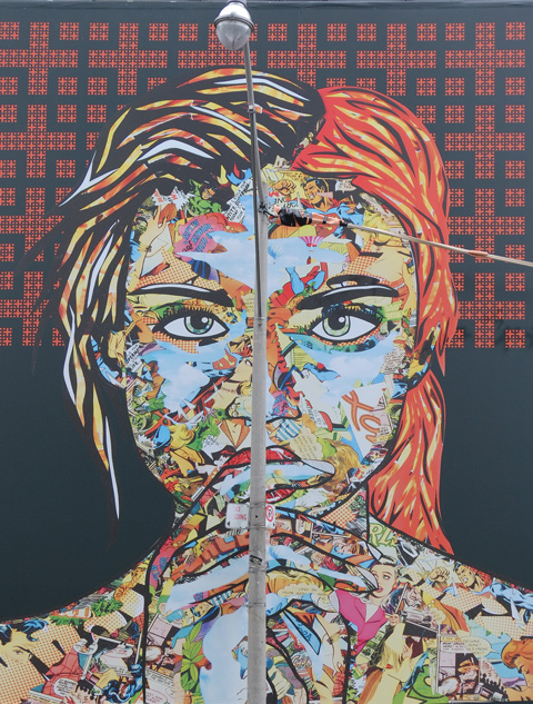 large maural by Daniel Mazzone, on construction hoardings, a woman's face and head, created by a collage of smaller images