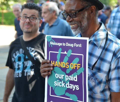 labour Day parade on Queen St West, an older black man carries a sign that says Hands Off our paid sick days 