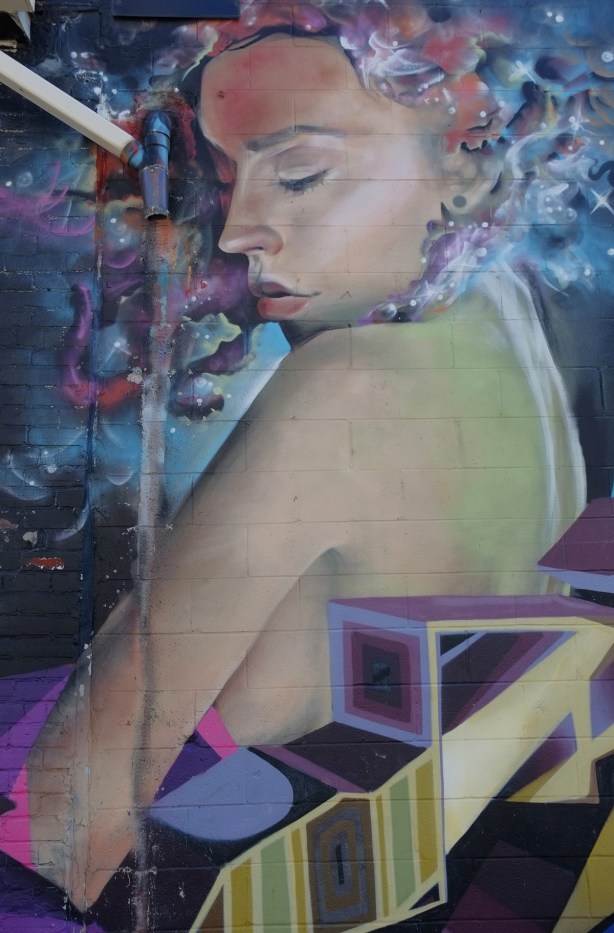 mural by jarus in an alley, a woman looking over her shoulder