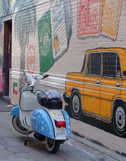 part of a mural in a narrow alley in Kensington by Dave Setrakian, a parrot on a perch and an airplane, a blue and white scooter, motorbike, is parked beside the mural 