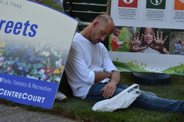 a man has fallen asleep on the grass beside the OPen Streets Park sign, 