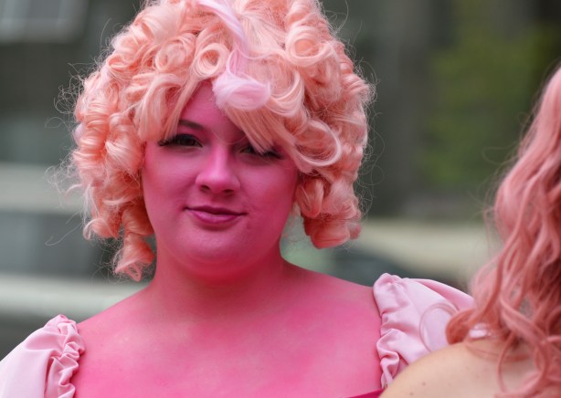 a woman in pale pink wig and totally covered face with pink paint