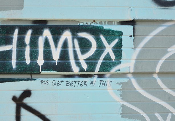 graffiti on a garage door, someone has written "pls get better at this" beside the scrawled graffiti 