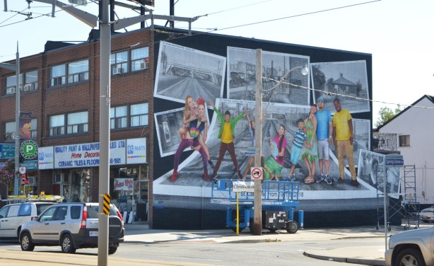 looking diagonally across the intersection of St. Clair West and Spring Grove Rd to a new mural that has just been finished on the side a building, painted by Christiano De Araujo. 