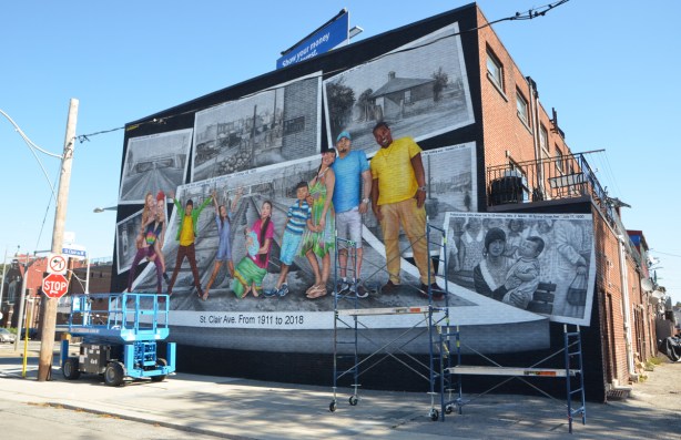 new mural on the side of a 2 storey building, a series of vintage black and white photos of the area and people, with paintings of 8 modern people in colour