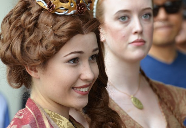 two women in costume, the one in front is smiling, the other is not, hair in braids, small crown on head,