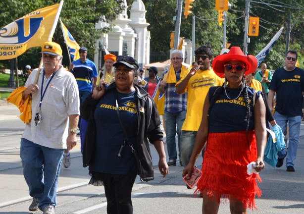 members of United Steelworkers walk in Labour Day parade including a woman in red cowboy hat and red frilly skirt 