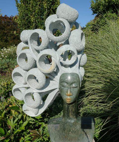 sculpture of a woman's head, eyes closed, with lots of rings of lighter stone hair, title is Windy Day 