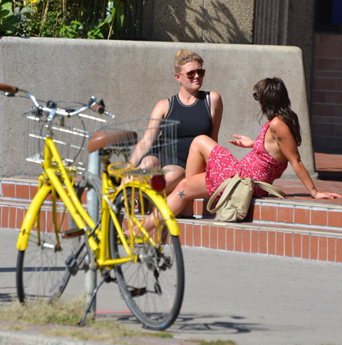two women sitting on the steps of a building having a discussion, a yellow bike is in the foreground 