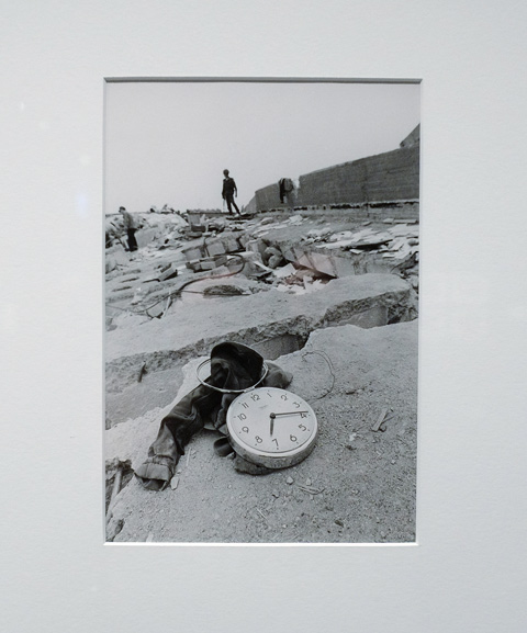 an old black and white photograph of Mexico city after the 1985 earthquake, a pair of pants and a clock on top of a flattened building, some people in the distance
