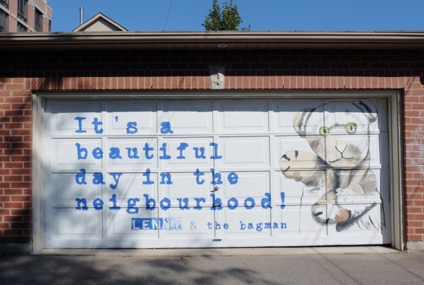 white garage door with blue words that say It's a beautiful day in the neighbourhood, also a picture of a hand puppet, 