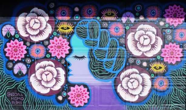 blue lady in profile, head only, with long hair ties up on head in a large braid, surrounded by stylized flowers in a mural in pinks and blues