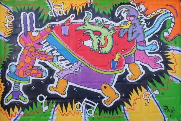mural by Al Runt, coloured creatures. a patchwork dog plays a piano that has walking legs