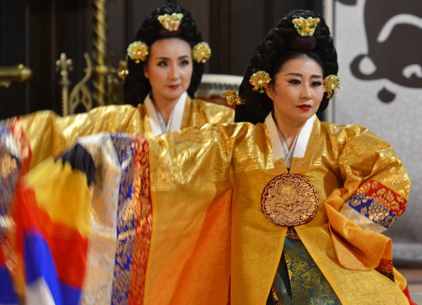 two Korean women in traditional costume, gold dresses, and decorated hair