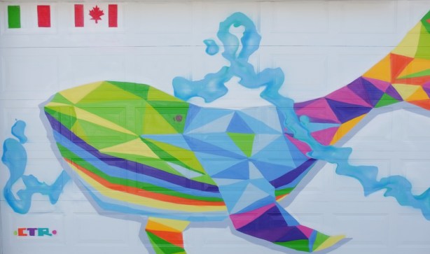 large mural of a many coloured whale swimming on a white garage door in an alley