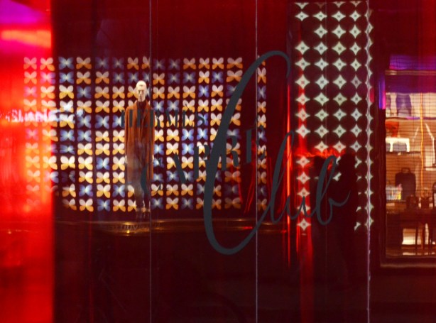 reflections in a window that has been lit with a red light, a mannequin is reflected from the store across the street
