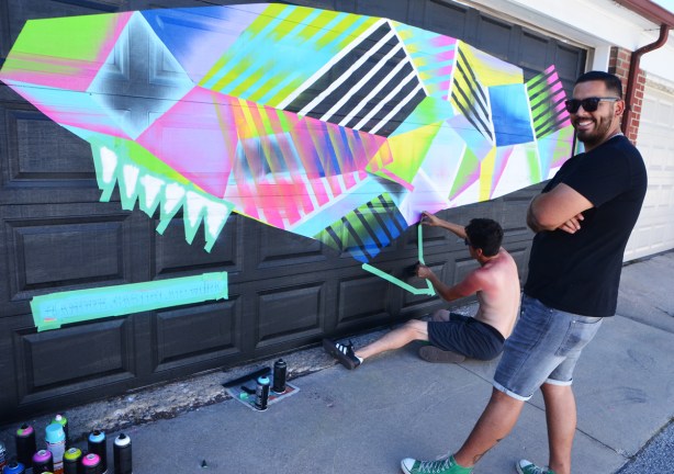 Andre Castro painting a mural of multicoloured whale on a garage door in a lane