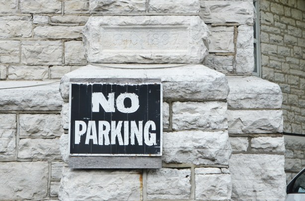 old black and white no parking sign on the side of a stone church, with engraved stone above it that says A.D. 1897