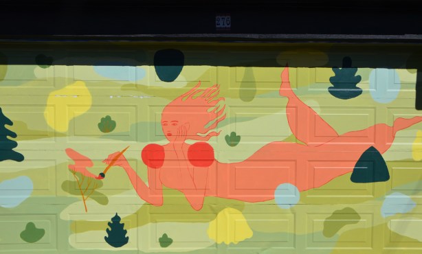 orange woman lying on the ground, holding a paint brush, mural on a garage door 