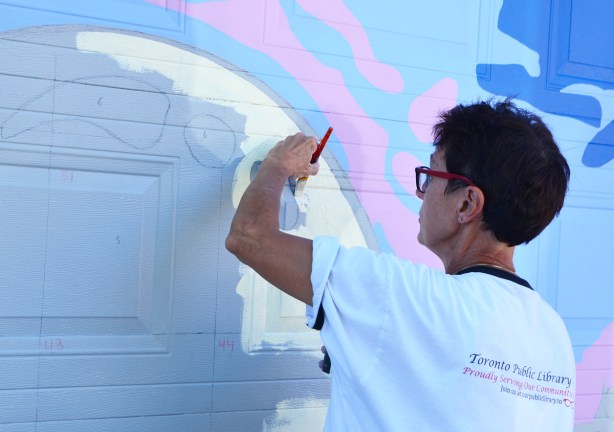a woman painting a mural on a garage door in an alley 