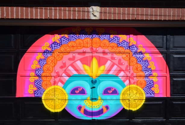 mural by muisca on garage door, bright colours, aztec face and head dress