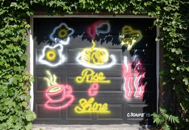 rise and shine mural by C. Scaife, looks like neon signs that would be in a restaurant, eggs cooking, hot coffee, bacon and the words rise and shine in cursive writing 