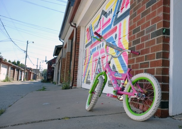a pink kids' bike parked beside a garage door with a mural, no seat on the bike 