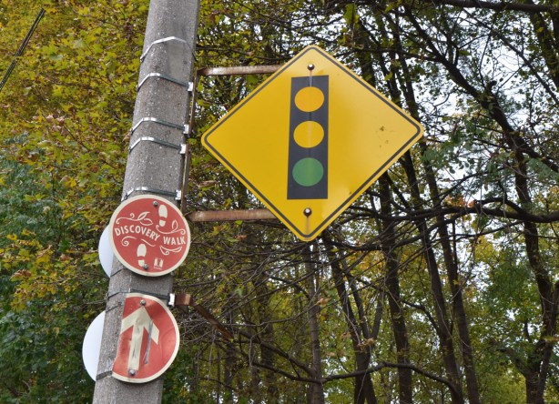 trees and woods behind, a yellow diamond shaped sign with picture of stoplight, telling people that there is a traffic signal ahead, except that the red light has faded and disappeared