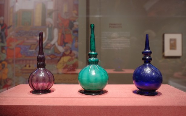 on display at the Aga Khan Museum, 3 glass bottles, rounded bottoms and narrow tops, one is marroon, one is teal and the last is royal blue