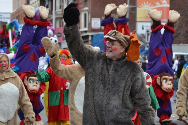 a man in a fuzzy grey animal costume waves to the crowd on the sidewalk at the Santa Claus parade 