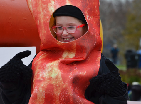 a child in red glasses is inside a bacon costume. 