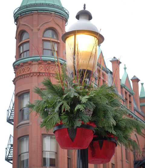 Christmas decorations, pine branches and red plant pots, on a lamp post in front of the Gooderham building in Toronto, red brick flatiron type building 
