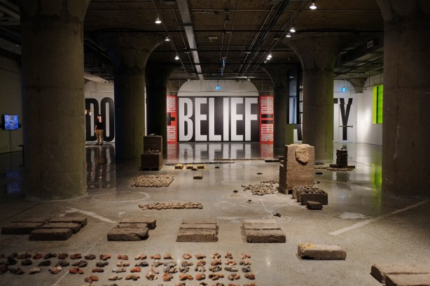 inside MOCA (Museum of Contemporary Art) which is an old industrial building, with original concrete columns, art installation on the floor and another on the far wall. On the wall are large words doubt, belief, and sanity. 