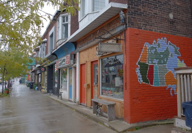 row of stores on Dundas Street, one on the end has a map of Canada painted on the exterior wall, with orange background. 