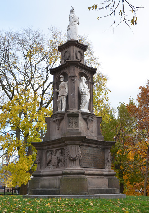 war memorial on a slight hill, grassy, in autum with yellow and orange leaves around, a white statue on top, with more statues (two) below.