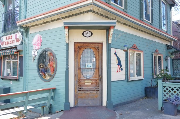 the front door of Park Snacks, a building on a corner, pale turquoise with lots of decorative finishes, a wood door, pink and cream coloured trim, 
