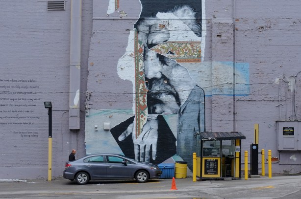 pale purple wall with mural and text, parkin lot attendent boothin front of wall as well as one parked car 