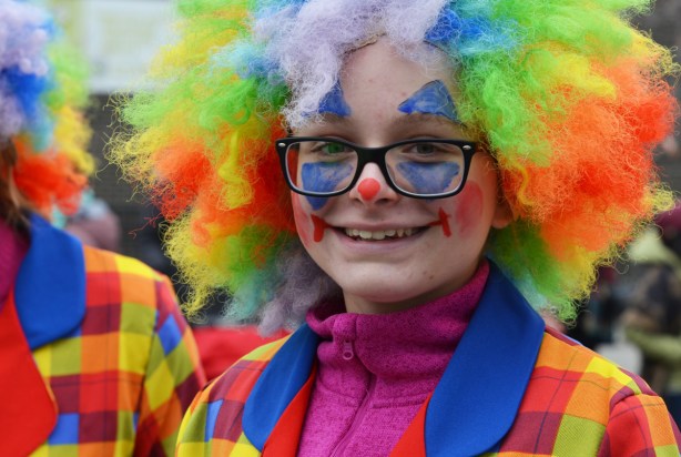 young woman with rainbow wig, and bright coloured clothes, clown in a parade 